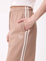 Pantalon de jogging de corte ancho, color negro con rayas laterales blancas. Posee cintura elastizada con cordón de ajuste y logo bordado en la parte frontal.