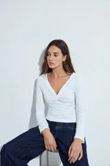 Top de manga larga blanco con escote en V y detalle de nudo fruncido en el centro del pecho.