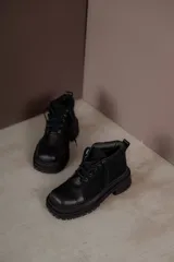 Borcegos de punta cuadrada con diseño acordonado, combinando paneles de cuero texturizado y gamuza en tonos marrones. Presentan una suela track gruesa de goma negra y cordones negros.