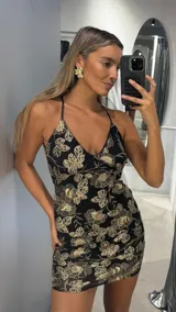 Vestido corto al cuerpo con escote en V y breteles finos. Presenta un diseño de flores bordadas en hilo dorado sobre una base de tul negro.