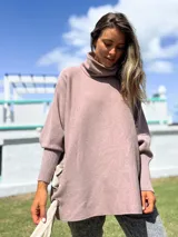 Polerón de cuello alto y corte oversize, color rosado, con mangas largas de puño acanalado y detalle de ojalillos metálicos con tiras en los laterales.