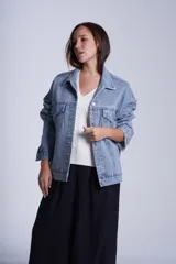 Campera clásica de jean celeste con cuello camisero, bolsillos frontales con solapa y cierre con botones metálicos. Presenta detalles de pequeños brillos blancos dispersos en la parte delantera y las mangas.