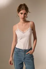 Body de breteles finos color blanco, con escote en V y detalle de encaje en el borde superior. Confeccionado en poliéster, presenta un diseño ajustado al cuerpo con cierre de broches en la parte inferior.