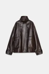 Chaqueta de cuero sintético con textura rugosa, cuello alto con trabilla, cierre frontal con cremallera y botones a presión, bolsillos delanteros y bajo ajustable con hebilla metálica.