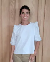 Remera blanca con cuerpo de algodón y mangas abullonadas de encaje bordado con detalles de volados en los hombros.