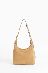 Cartera tipo hobo de cuero color camel, con diseño holgado y cierre superior. Presenta un detalle metálico en la parte superior y el logo de la marca grabado en el frente.