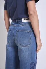 Pantalón de jean azul con bordados florales y aberturas en forma de flor en las piernas.