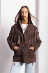 Campera marrón de gamuza con corte masculino, hombros marcados y caída recta. Tiene flecos largos en la espalda y mangas.