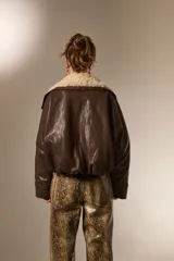 Chaqueta de cuero sintético color marrón, con cuello de piel sintética en tono crema, cierre frontal y diseño holgado.