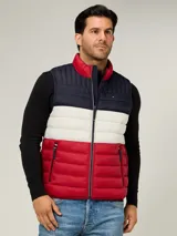 Chaleco acolchado de diseño color block con franjas horizontales en azul marino, blanco y rojo. Presenta cuello alto, cierre frontal de cremallera y dos bolsillos laterales con cierre. Incluye logo de la marca bordado en el pecho.