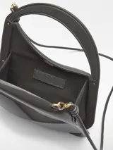 Bolso de cóctel Adolfo Domínguez de estructura rígida y acabado brillante. Presenta un diseño asimétrico con asa tubular integrada y correa larga extraíble. Cuenta con cierre magnético y logo de la marca estampado en dorado.