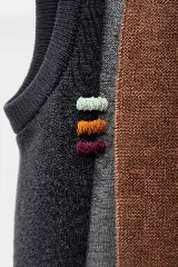 Chaleco abierto de lana, con diseño de bloques de color verticales en tonos marrón, gris y negro. Presenta un detalle de bordado artesanal con tres líneas horizontales en el frente y un ajuste holgado.