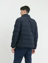 Campera capitoneada de poliéster color negro, con capucha desmontable, cierre frontal y bolsillo en el pecho con cierres engomados y tiradores en color naranja.