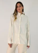 Camisa de algodón color crema, con cuello alto estilo victoriano con volados, cierre frontal de botones y mangas largas con puños clásicos.