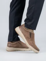 Zapato tipo slip-on Hush Puppies modelo Hunt, confeccionado en cuero color marrón con suela de EVA y goma en tono beige. Presenta elásticos laterales para facilitar el calce y un diseño de estilo casual.