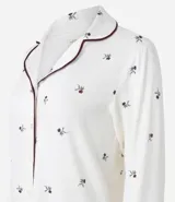Camisón estilo americano de corte recto, confeccionado en viscolycra color blanco con estampado de pequeñas flores oscuras. Presenta cuello clásico, cierre frontal con botones, mangas largas con puños y detalles de biés en contraste.