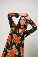 Vestido largo negro con estampado de flores naranjas y amarillas, cuello mao con abertura en forma de gota, mangas largas acampanadas con botones en los puños, tajo lateral y flecos en el ruedo.