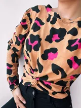 Remera de manga larga color beige con estampado animal print en negro y fucsia. Presenta cuello redondo y nudo decorativo en la parte delantera.