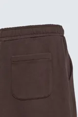 Pantalón jogger de algodón color marrón oscuro, de corte relajado y pierna ancha. Presenta cintura elástica con cordón ajustable y bolsillos laterales y uno trasero de plastrón.