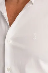 Camisa blanca de manga larga con cierre frontal de botones y detalle de logo bordado en el pecho.