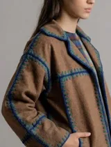 Chaqueta de paño de lana color marrón con detalles de costuras artesanales en crochet en color azul y verde. Presenta un diseño de corte recto y holgado con solapas.