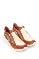 Zapatilla deportiva marrón de cuero liso con detalles en beige y plateado. Presenta cierre lateral y suela gruesa blanca.