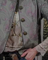 Chaqueta de pana color verde militar con estampado paisley, cuello mao, cierre frontal con botones metálicos y ribetes negros.