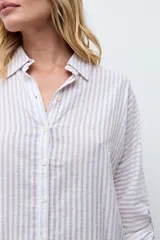 Camisa de corte holgado con diseño de rayas verticales en tonos beige y blanco, con sutiles destellos brillantes. Presenta cuello clásico, cierre frontal con botones y mangas largas con puños ajustables.