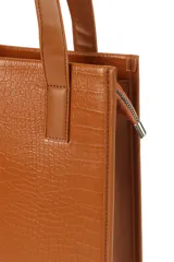 Bolso tipo tote de diseño estructurado y formato vertical, confeccionado en cuero sintético con textura grabada tipo cocodrilo. Cuenta con doble asa de hombro y cierre lateral.