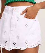 Short pollera corto de jeans blanco con bordados calados (cutout) y bajo festoneado. Presenta trabillas en la cintura y cierre tradicional.