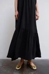 Vestido midi de color negro, confeccionado en tejido fluido, con escote en V y tirantes finos ajustables. Presenta frunces en el pecho y un volante en el bajo.