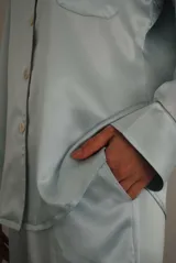 Pijama de satén elastizado color celeste, compuesto por una camisa de manga larga con cuello solapa, botones frontales y bolsillo en el pecho, y un pantalón recto con cintura elástica y lazo ajustable.