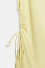 Vestido midi confeccionado en hilatura de algodón de color amarillo, con cuello redondo, manga corta y detalles de frunces laterales ajustables con cordones. Presenta bajo asimétrico con acabado en línea evasé.