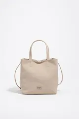 Bolso shopper mediano de nylon color beige con estructura blanda, doble asa corta de mano y correa fina ajustable. Cuenta con cierre de botón a presión, bolsillo interior con cierre y aplique metálico con el logo de la marca en el frente.