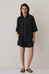 Camisa negra de manga corta, con cuello camisero, cierre frontal de botones y un bolsillo aplicado en el pecho.