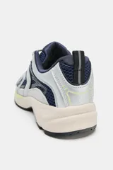 Zapatilla deportiva estilo running con combinación de materiales y colores. Presenta paneles en azul marino, plateado y detalles en amarillo neón, con suela de plataforma en tono beige y tirador en el talón.