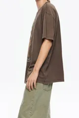 Camiseta de algodón orgánico color negro con efecto gastado, corte oversize y manga corta ancha. Presenta un estampado artístico enmarcado con el texto "BIMBA Y LOLA" en la parte superior e inferior.