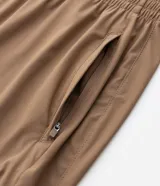 Pantalón deportivo de corte recto, color marrón, con cintura elástica y cordón de ajuste. Presenta bolsillos laterales con cierre y un diseño minimalista de tejido técnico.