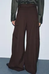 Pantalón ancho de tiro medio color marrón oscuro, confeccionado en tejido con lana. Presenta pinzas delanteras, cinturón ajustable con hebilla metálica y bolsillos cargo de plastrón en las piernas.