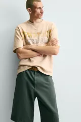 Camiseta relaxed fit de punto color beige con efecto lavado, cuello redondo y manga corta. Cuenta con estampado frontal con texto en tonos amarillo, azul y rojo.