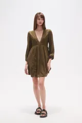 Vestido corto de color verde militar, con escote en V profundo, mangas largas con puños elásticos y detalles de encaje y bordados en el frente. Presenta una falda con vuelo y textura de pequeños puntos en relieve.