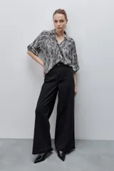 Jean wide leg negro de tiro alto, confeccionado en denim rígido, con diseño de cinco bolsillos, presillas para cinto, cierre frontal con botón y ruedo desflecado.