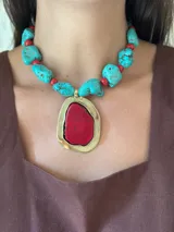 Collar corto con piedras rojas engarzadas en metal dorado y cuentas de magnesita turquesa intercaladas. El dije principal es una piedra roja de forma irregular engarzada en metal dorado.