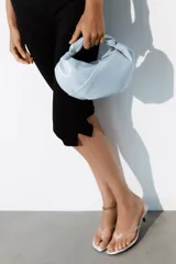 Bolso de mano celeste de diseño fruncido, con asa superior retorcida y cadena metálica dorada estilo bandolera. Cuenta con cierre de cremallera.