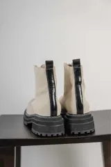 Botas de caña corta color beige, confeccionadas en cuero con textura granulada. Presentan cierre frontal central, suela track negra de goma con costuras blancas visibles y tirador en la parte trasera.