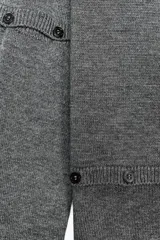 Jersey de punto gris oscuro, cuello redondo y manga larga. Presenta detalles desmontables con botones a lo largo de las costuras de las mangas y en el ruedo inferior.