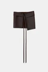 Cinturón tipo falda confeccionado en piel 100% color marrón oscuro, con diseño envolvente y cierre mediante lazada frontal.