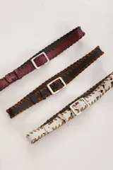 Cinturón de cuero color bordó con costuras de tientos en color azul oscuro a lo largo de los bordes. Posee una hebilla rectangular metálica plateada.