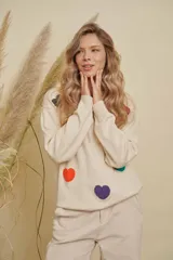 Buzo de punto color crema con diseño de corazones de colores aplicados en relieve, cuello redondo y mangas largas con puños acanalados.