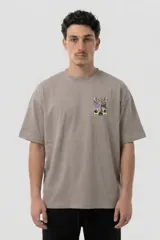 Remera de algodón color gris topo con corte relajado. Presenta un diseño gráfico estampado en la espalda que combina una figura abstracta con parlantes en tonos violeta y verde ácido.